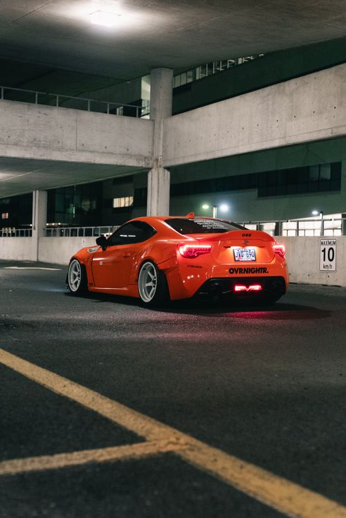 Free Sleek orange sports car parked in a dimly lit urban environment at night, exuding modernity. Stock Photo