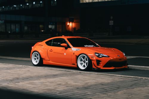 Free A sleek orange sports car parked on a city street at night, showcasing its vibrant color and sporty design. Stock Photo