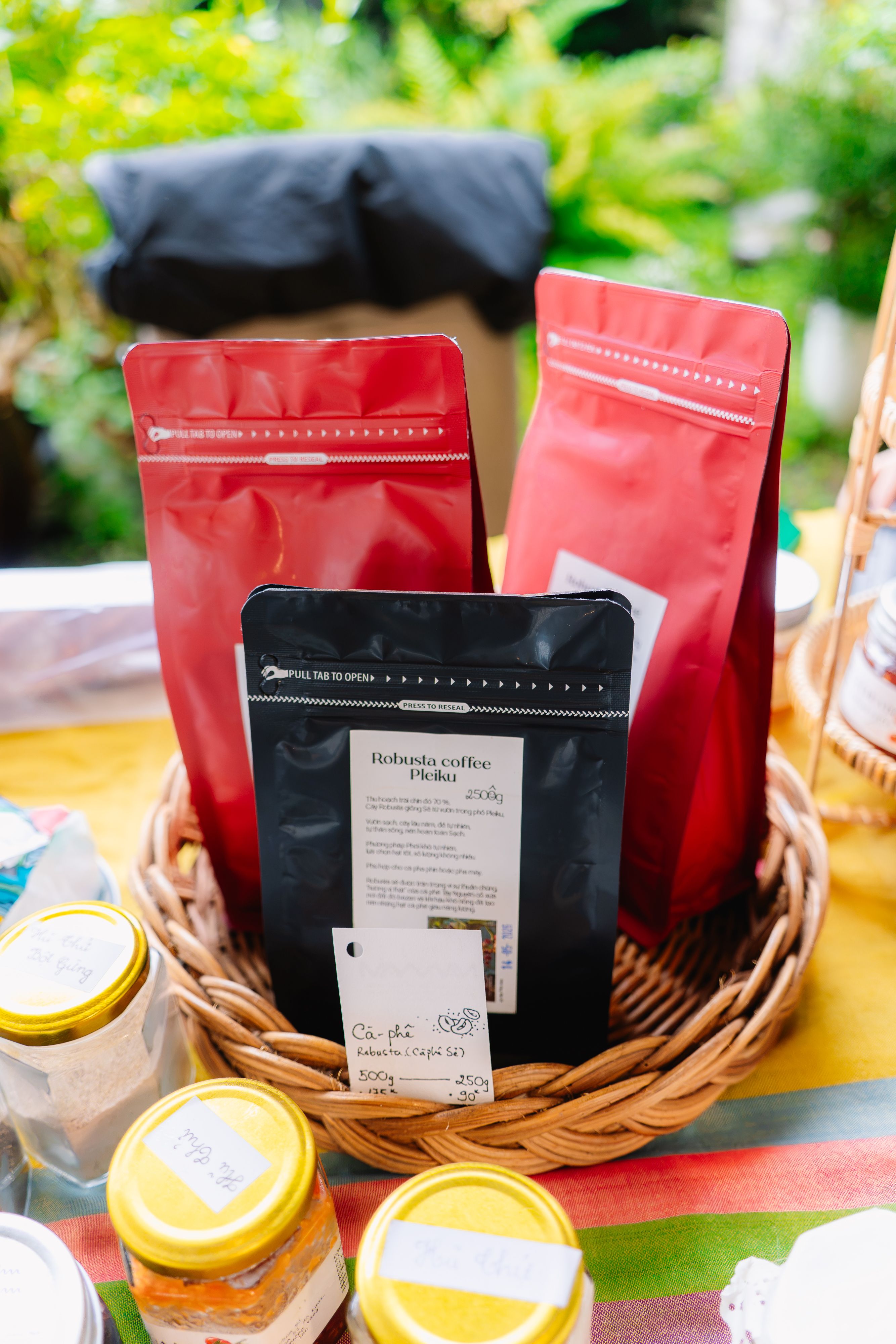 Three colorful coffee bags displayed in a wicker basket at an outdoor market stand.