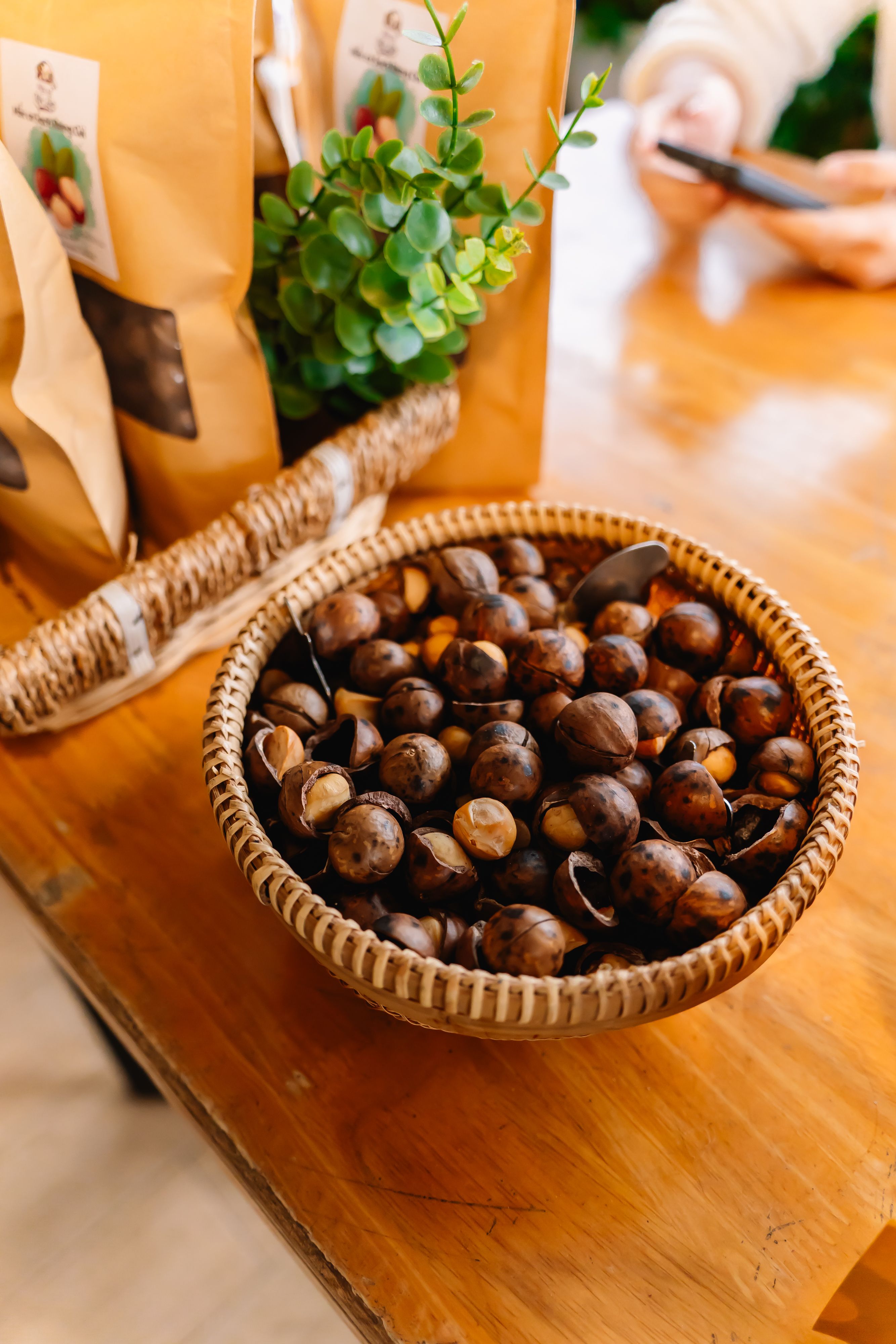 A wicker basket filled with macadamia nuts on a wooden table indoors, natural lighting.