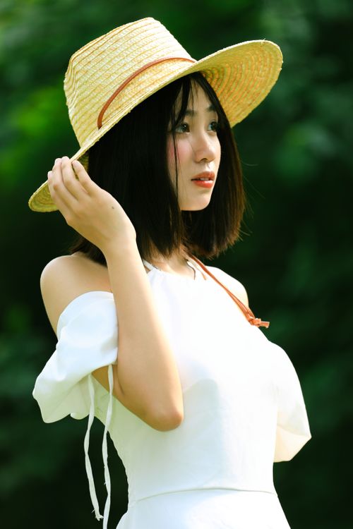 Free Charming young woman in a white dress wearing a straw hat outdoors in Hanoi, Vietnam. Stock Photo