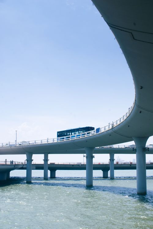 Free A blue bus travels across a sleek, curved bridge over calm waters under a clear sky. Stock Photo