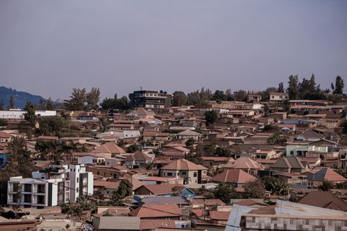 Free Scenic aerial view of dense urban rooftops against a picturesque hilly backdrop under a clear sky. Stock Photo
