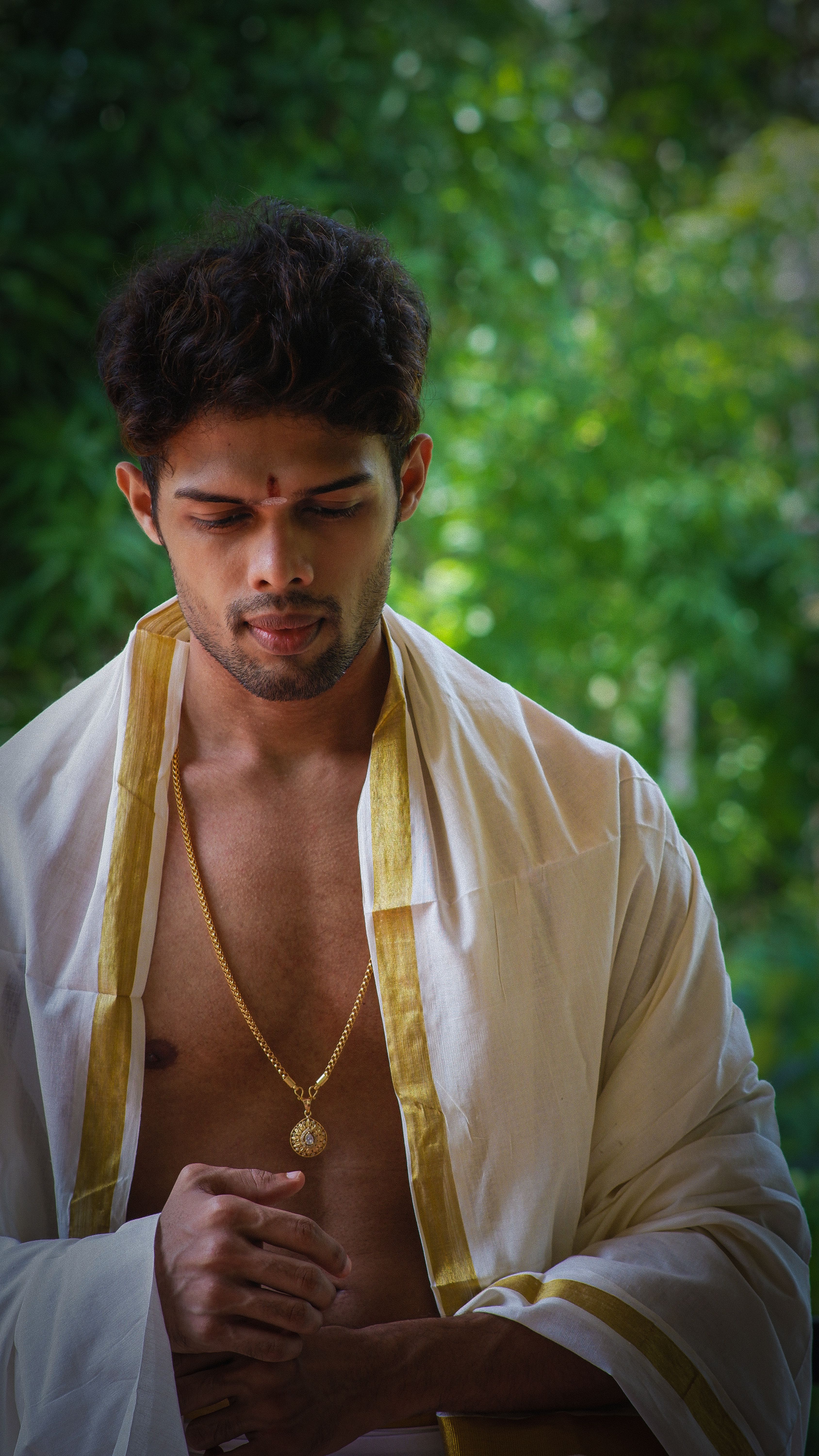 Young man in traditional Indian attire standing against a lush green background.