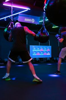 Men engaged in boxing training with punching bags in a modern gym setting.