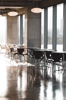 Modern cafe with empty tables and large windows casting sunlight.