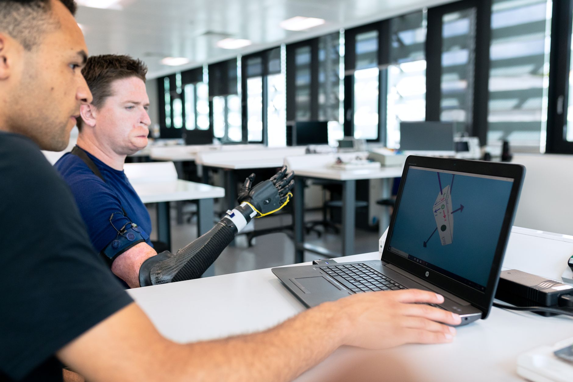 Two engineers collaborate on prosthetic design using a laptop, focusing on technological innovation.