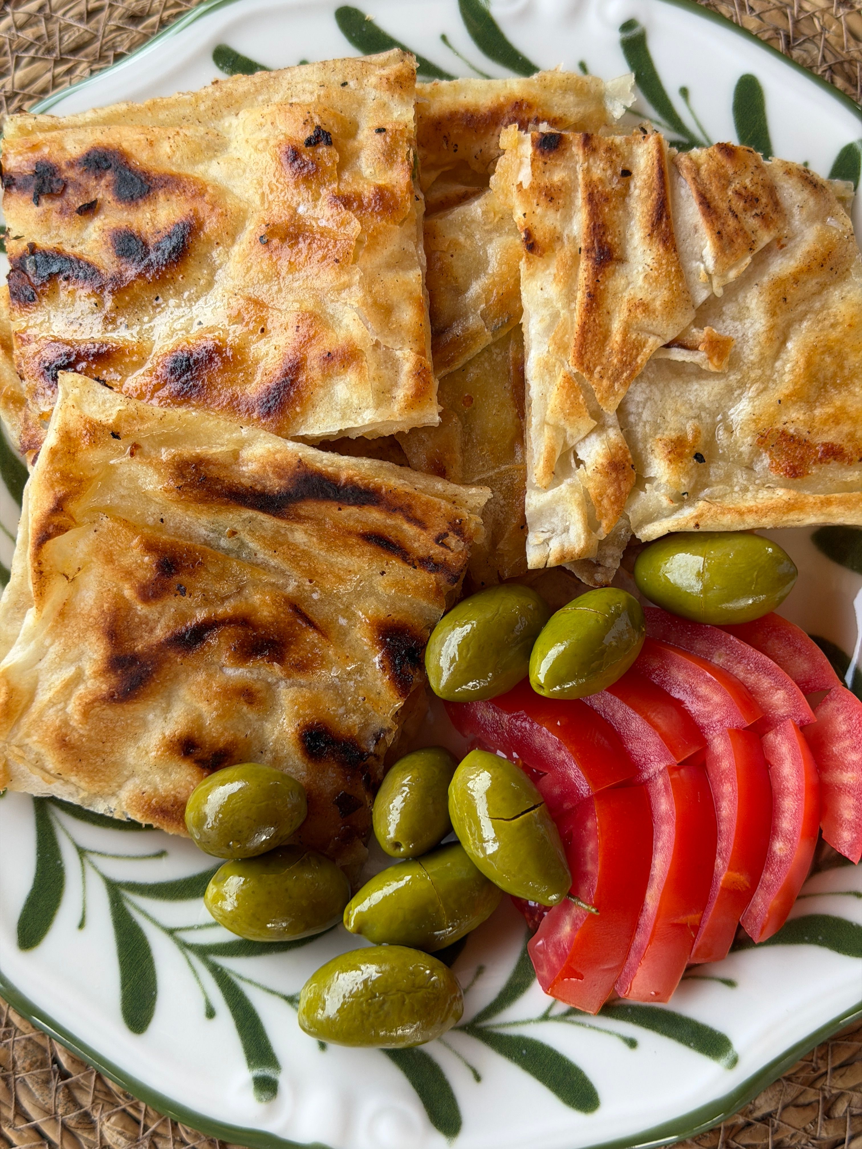 A savory Turkish breakfast featuring gözleme, olives, and fresh tomato slices.