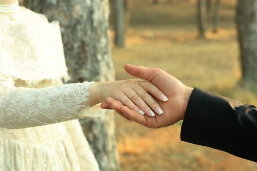 Free Close-up of a couple holding hands in a romantic outdoor setting, symbolizing love and commitment. Stock Photo