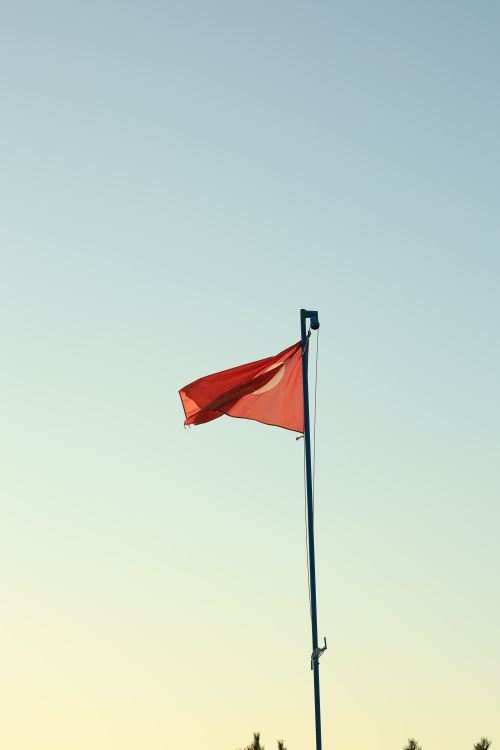 Free A vibrant red flag waves against a clear sky, symbolizing caution or alertness. Stock Photo