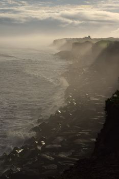 Dramatic misty cliffs along a serene coastline at sunrise.