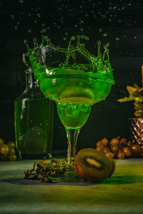 Free Vivid green kiwi cocktail splash in a margarita glass, surrounded by fresh fruits and dim lighting. Stock Photo