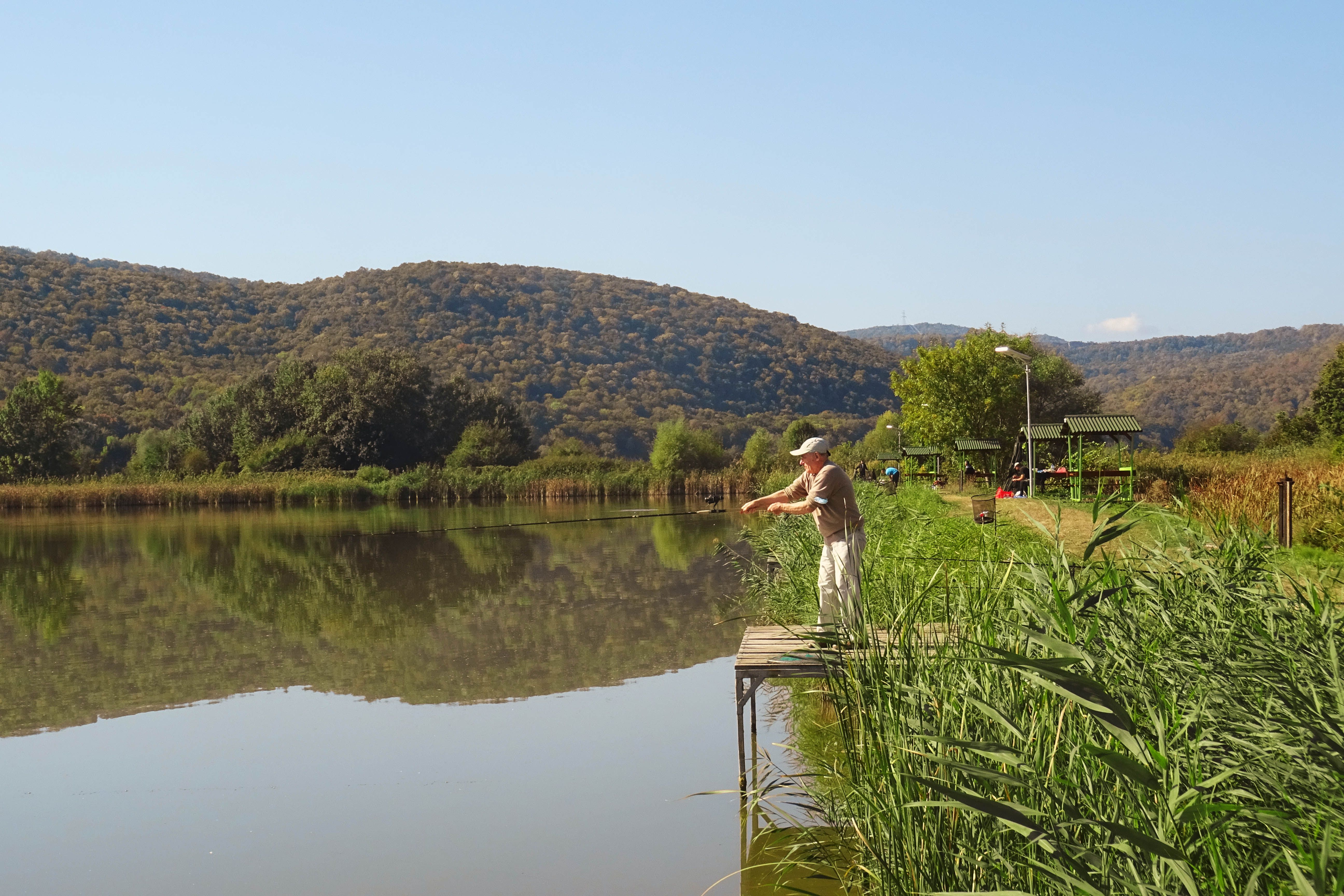 A person fishing on a peaceful lake surrounded by green hills