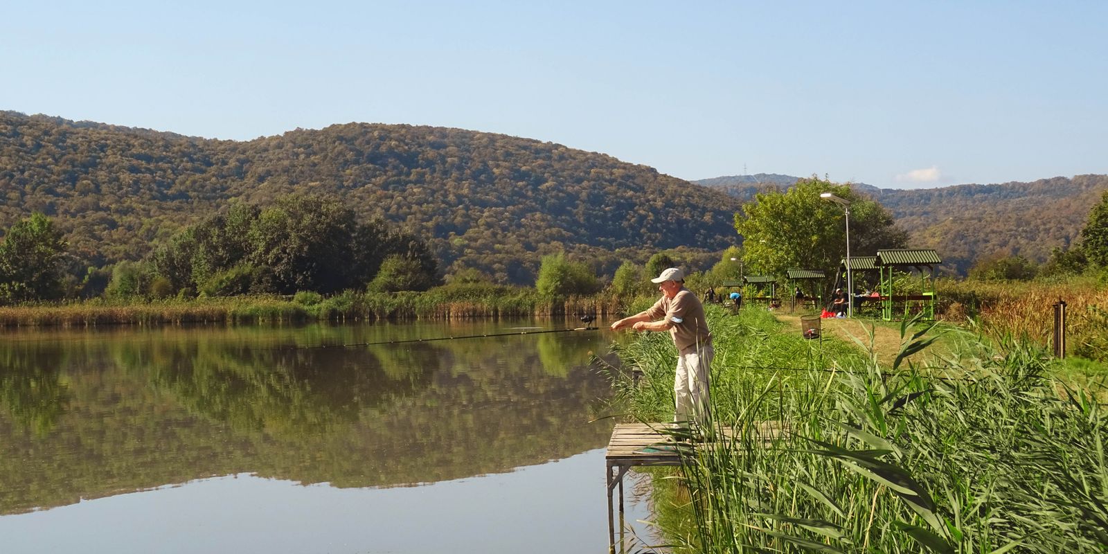 A person fishing on a peaceful lake surrounded by green hills
