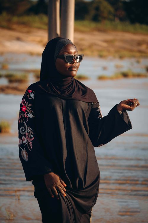 Free Fashionable woman in hijab and sunglasses standing by a riverbank in sunny weather. Stock Photo