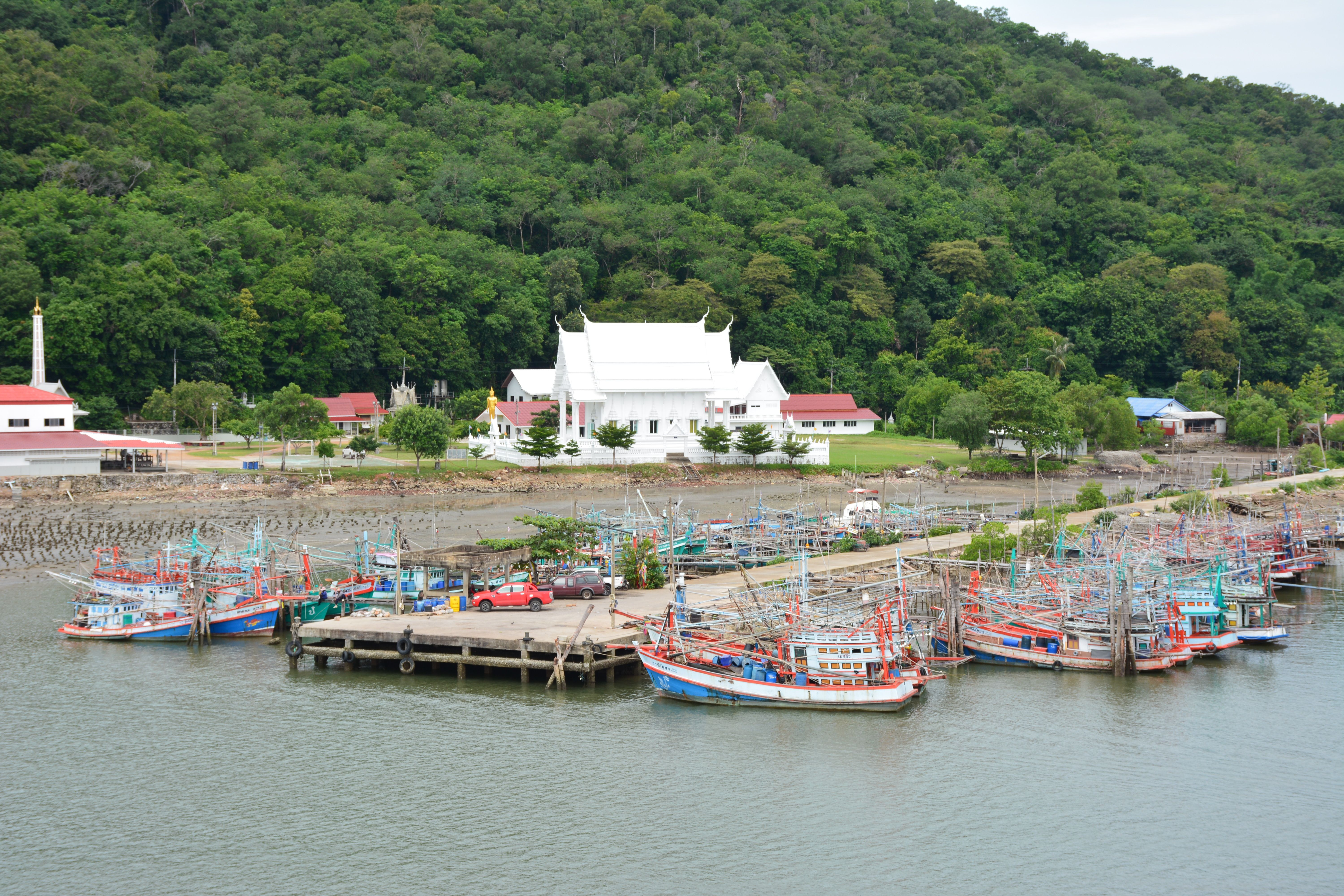 Colorful fishing boats docked with a temple in the background in Chanthaburi, Thailand.