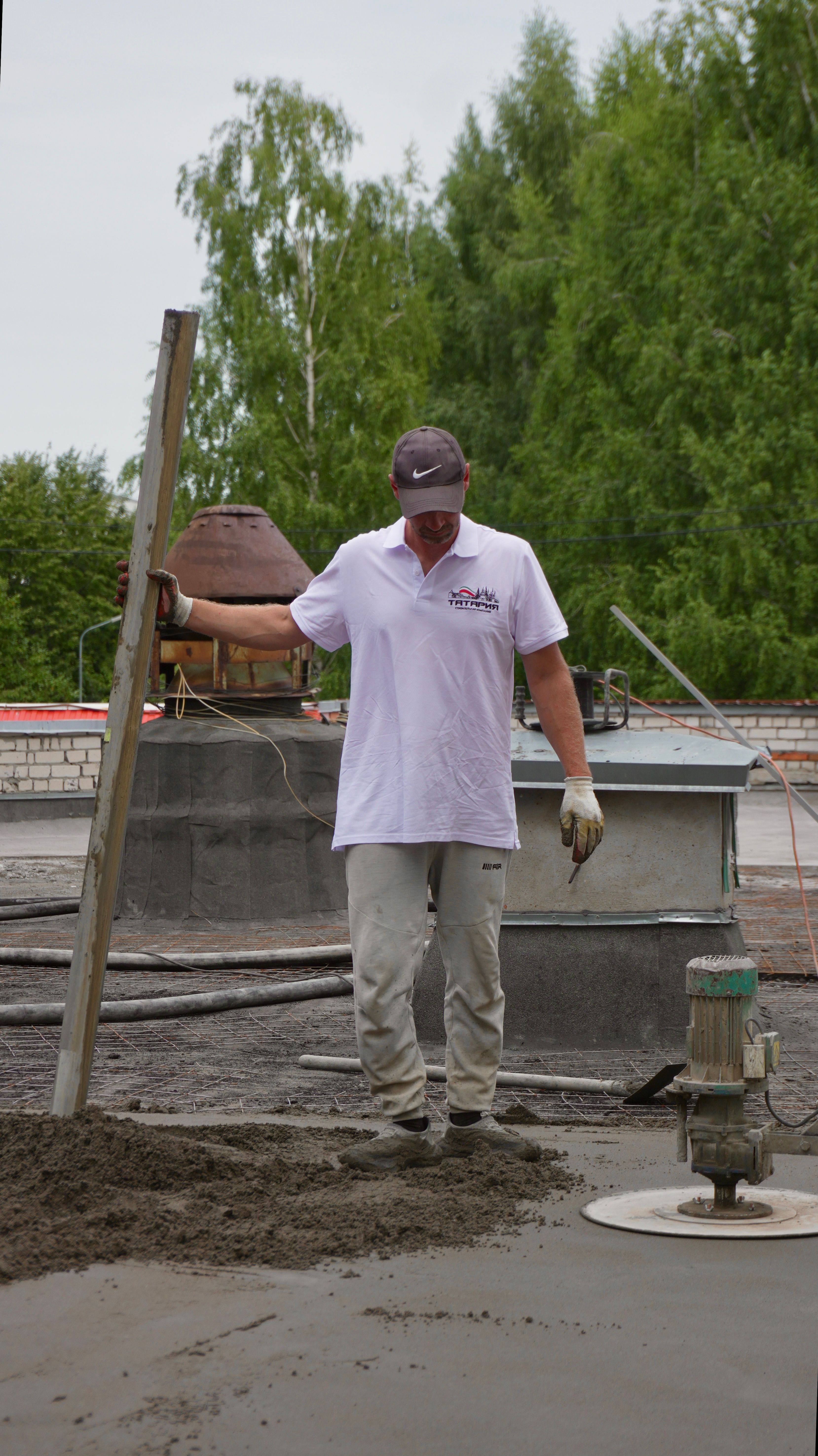 Construction worker in casual attire leveling freshly poured concrete outdoors at a site.