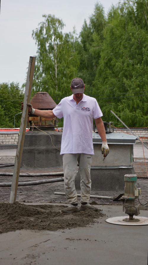 Free Construction worker in casual attire leveling freshly poured concrete outdoors at a site. Stock Photo