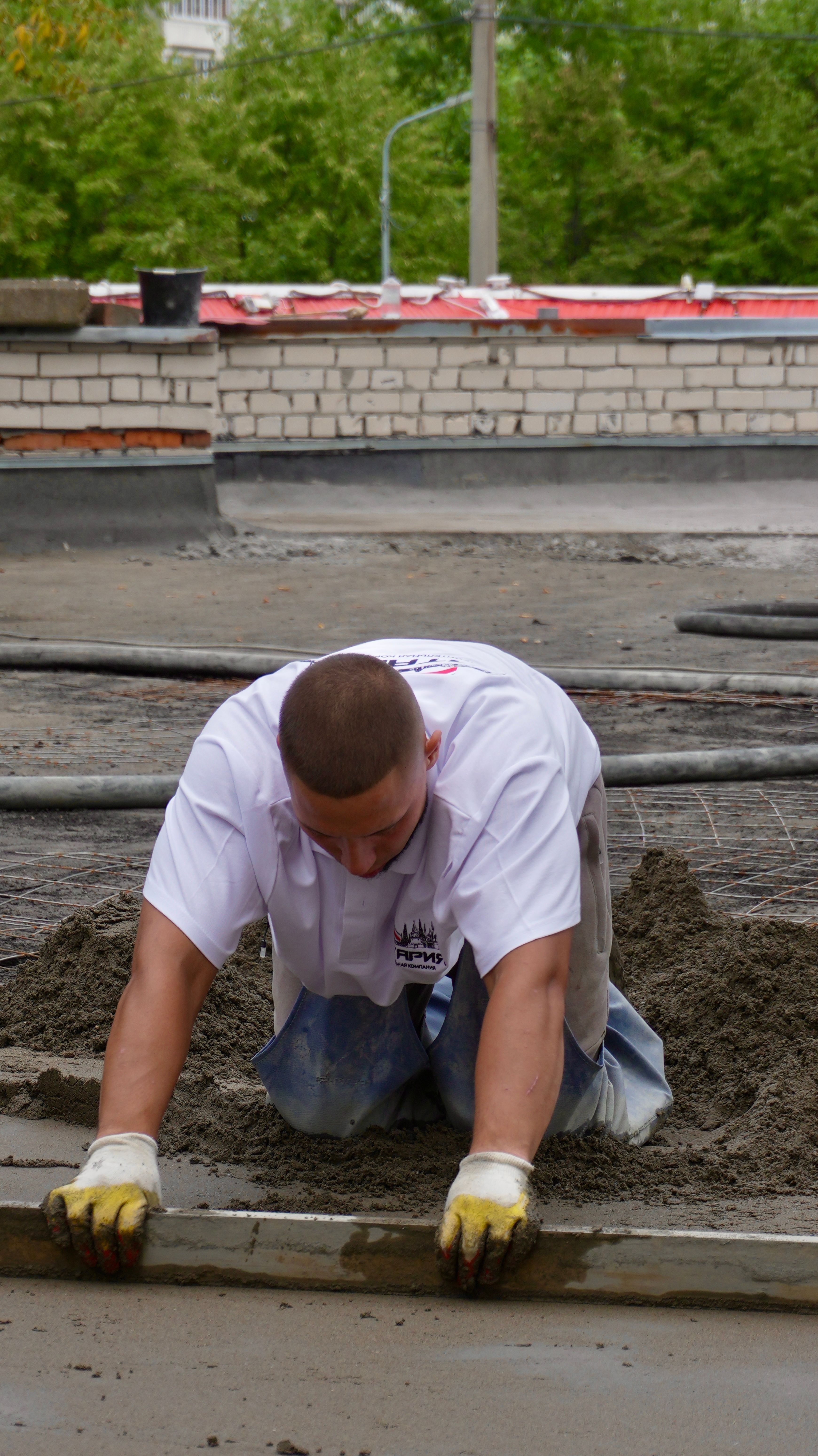 A construction worker spreads concrete at an outdoor site wearing safety gloves.