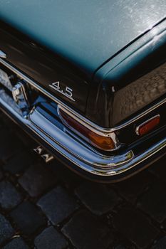 Close-up of a classic 4.5 car's rear showcasing chrome details and tail lights, parked on a cobblestone street.