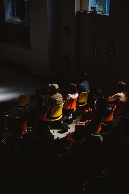 Free A group of people seated in a dimly lit room in Berlin, highlighting contrasting shadows. Stock Photo