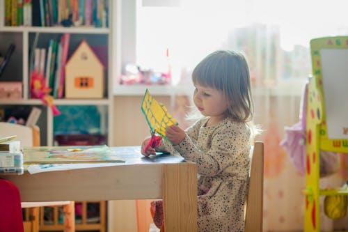 Meisje In Witte Jurk Met Lange Mouwen Zittend Op Bruin Houten Stoel Snijden Papier