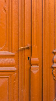 Close-up of an orange vintage wooden door with ornate carvings and a keyhole.