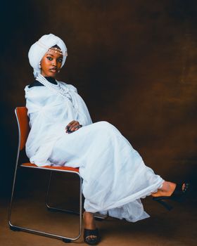 A woman in traditional Nigerian clothing seated gracefully on a chair.