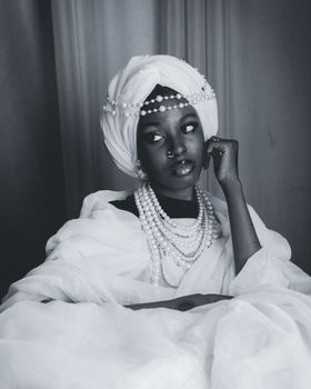 A striking black and white portrait of an African woman adorned in pearls and traditional attire, exuding elegance.