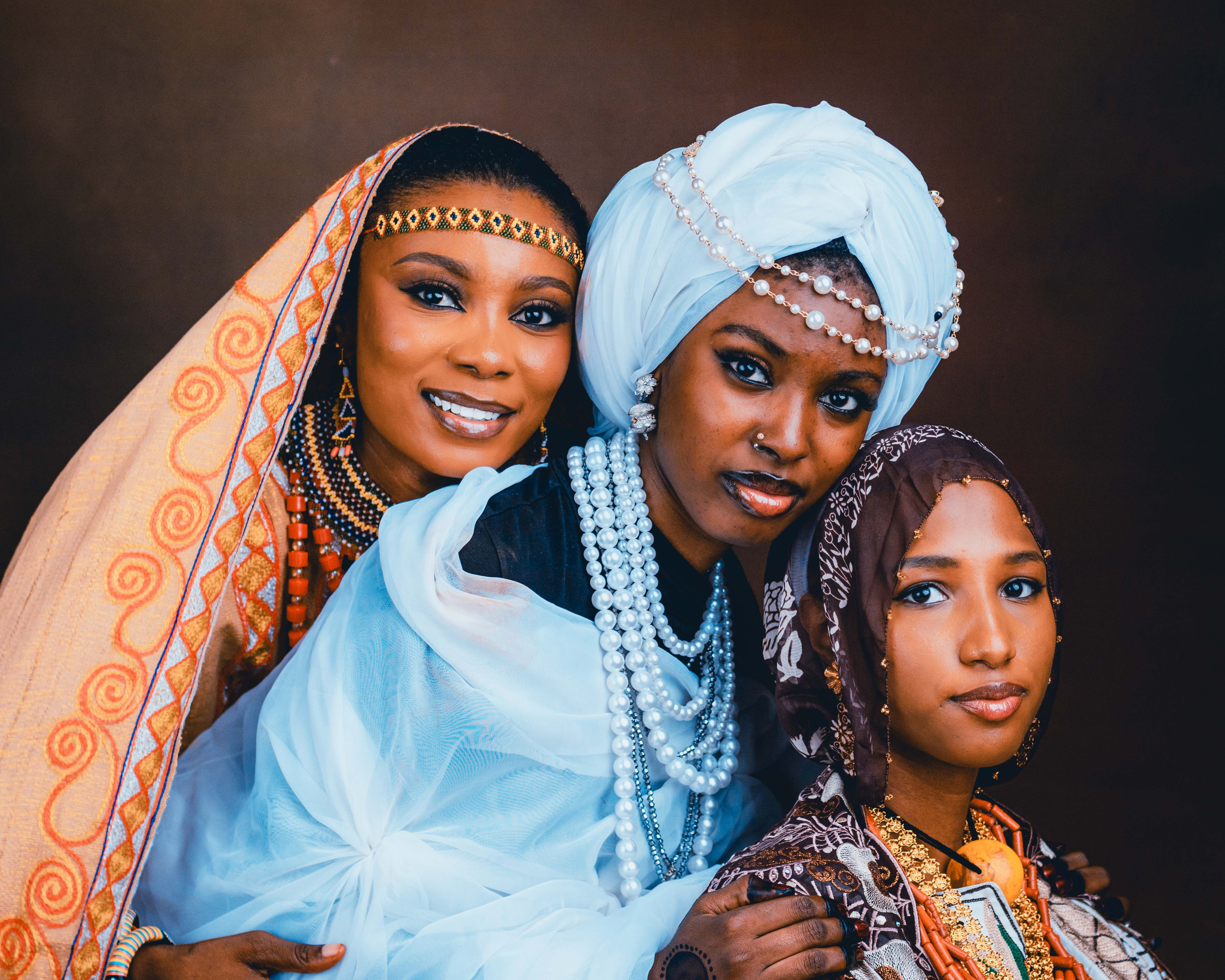 Elegant portrait of three African women wearing traditional and contemporary outfits adorned with jewelry.