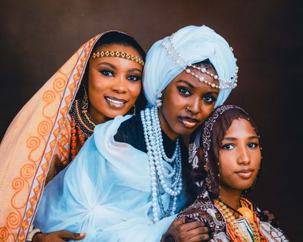 Elegant portrait of three African women wearing traditional and contemporary outfits adorned with jewelry.
