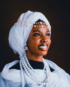 Portrait of a smiling African woman wearing traditional attire with pearl accessories.