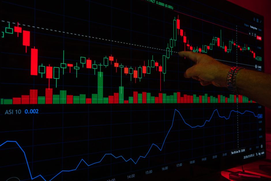 Una mano señala un gráfico bursátil en una pantalla digital, destacando las tendencias de las operaciones financieras.