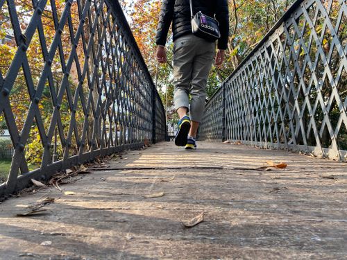 Free A person walks across a wooden footbridge surrounded by autumn leaves, creating a tranquil outdoor scene. Stock Photo