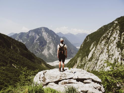 Free A lone traveler stands atop a cliff, overlooking a vast mountainous valley. Stock Photo