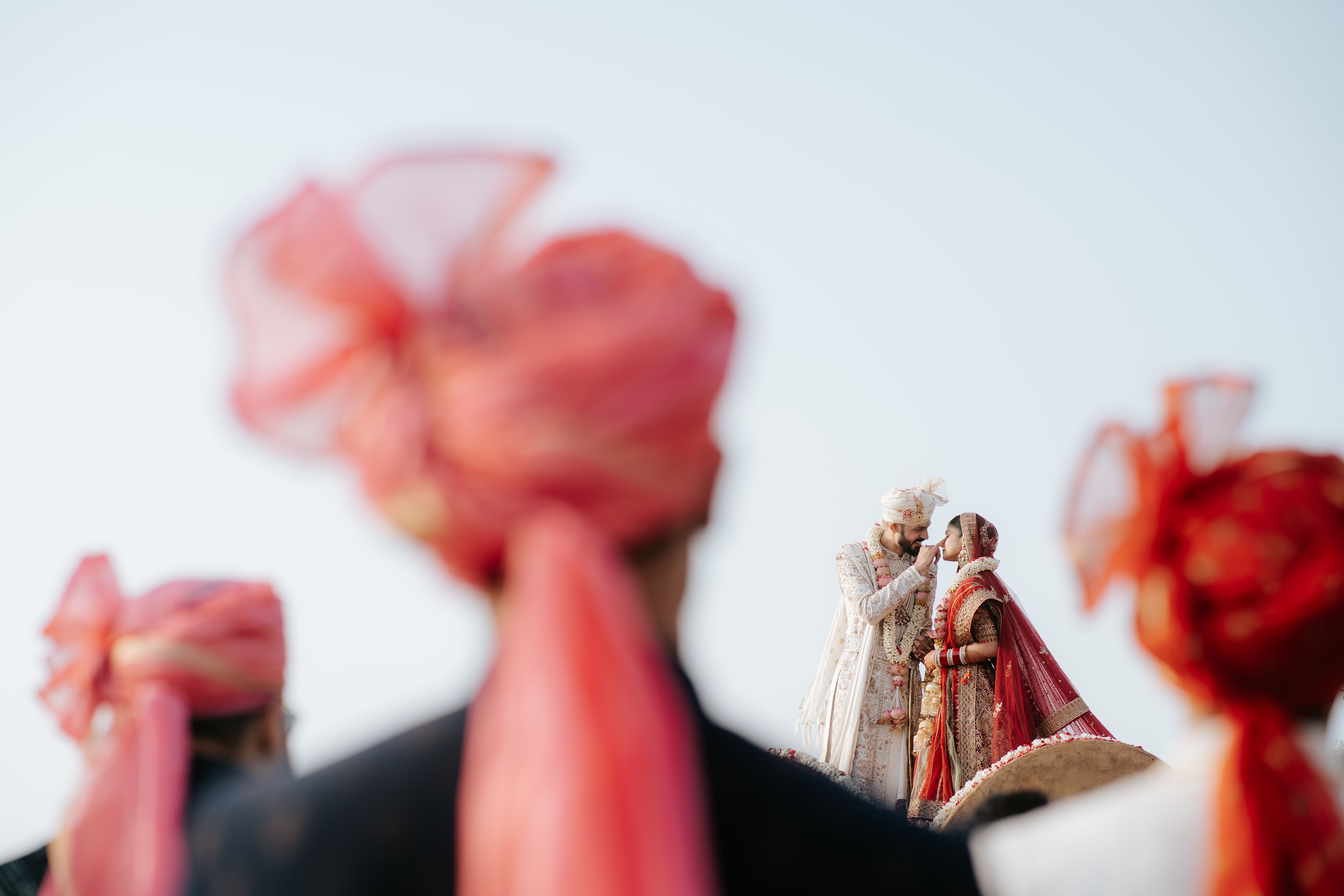 Beautiful moment captured at an outdoor Indian wedding featuring a couple in traditional attire with guests in focus.