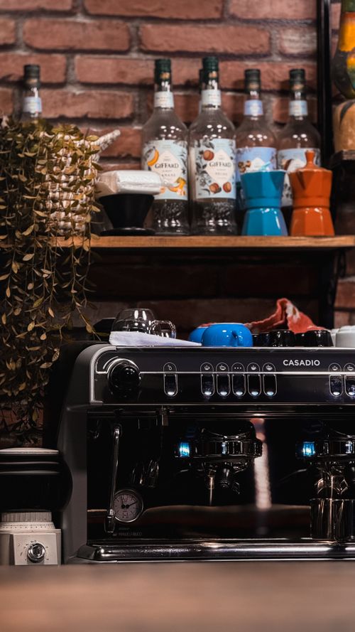 Free A sleek espresso machine in a rustic café, complemented by coffee accessories on a brick wall background. Stock Photo