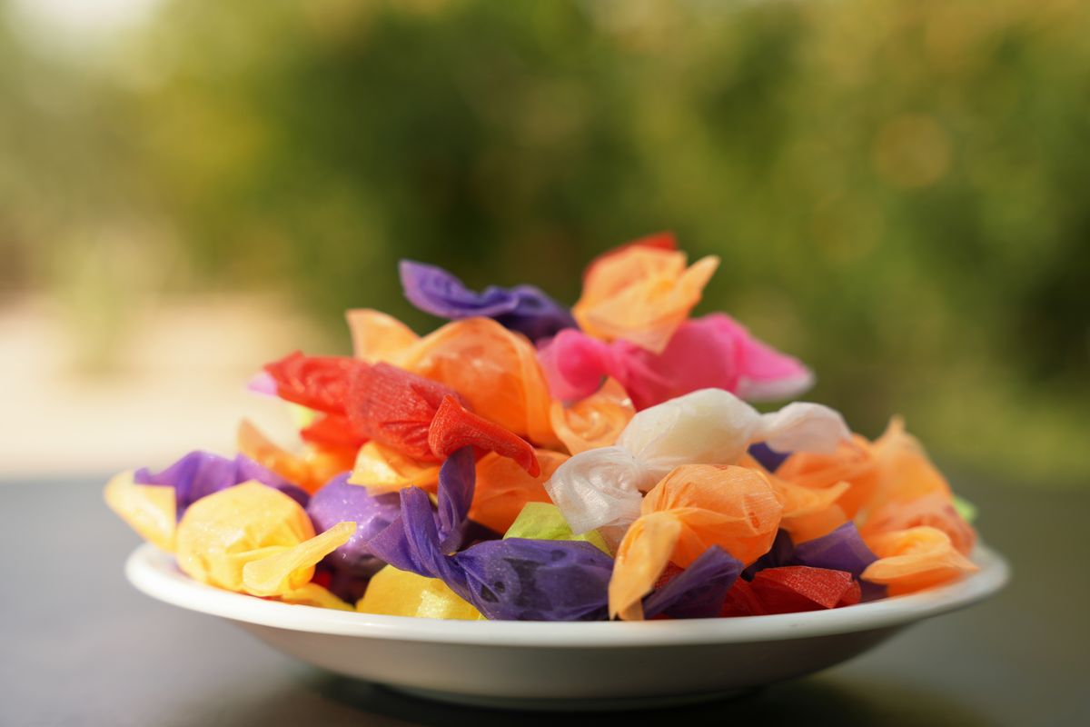 A vibrant pile of assorted wrapped candies in a white bowl outdoors.