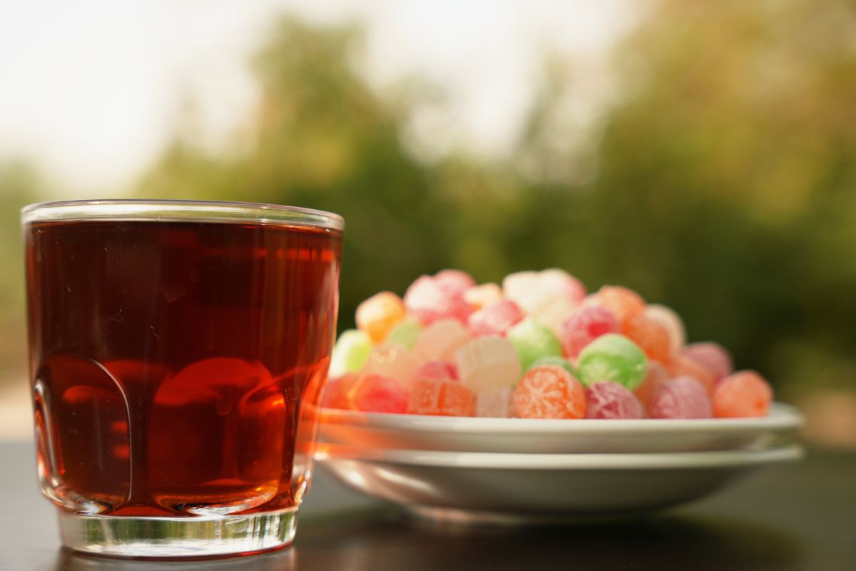 A glass of Persian tea with colorful sweets outdoors, perfect for a summer afternoon.