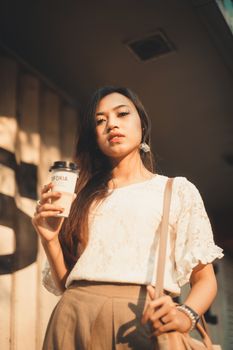 自信的女人端着咖啡杯，在户外享受阳光明媚的一天