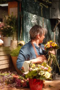 Florist arranging vibrant flowers into a bouquet at an outdoor flower market stall.