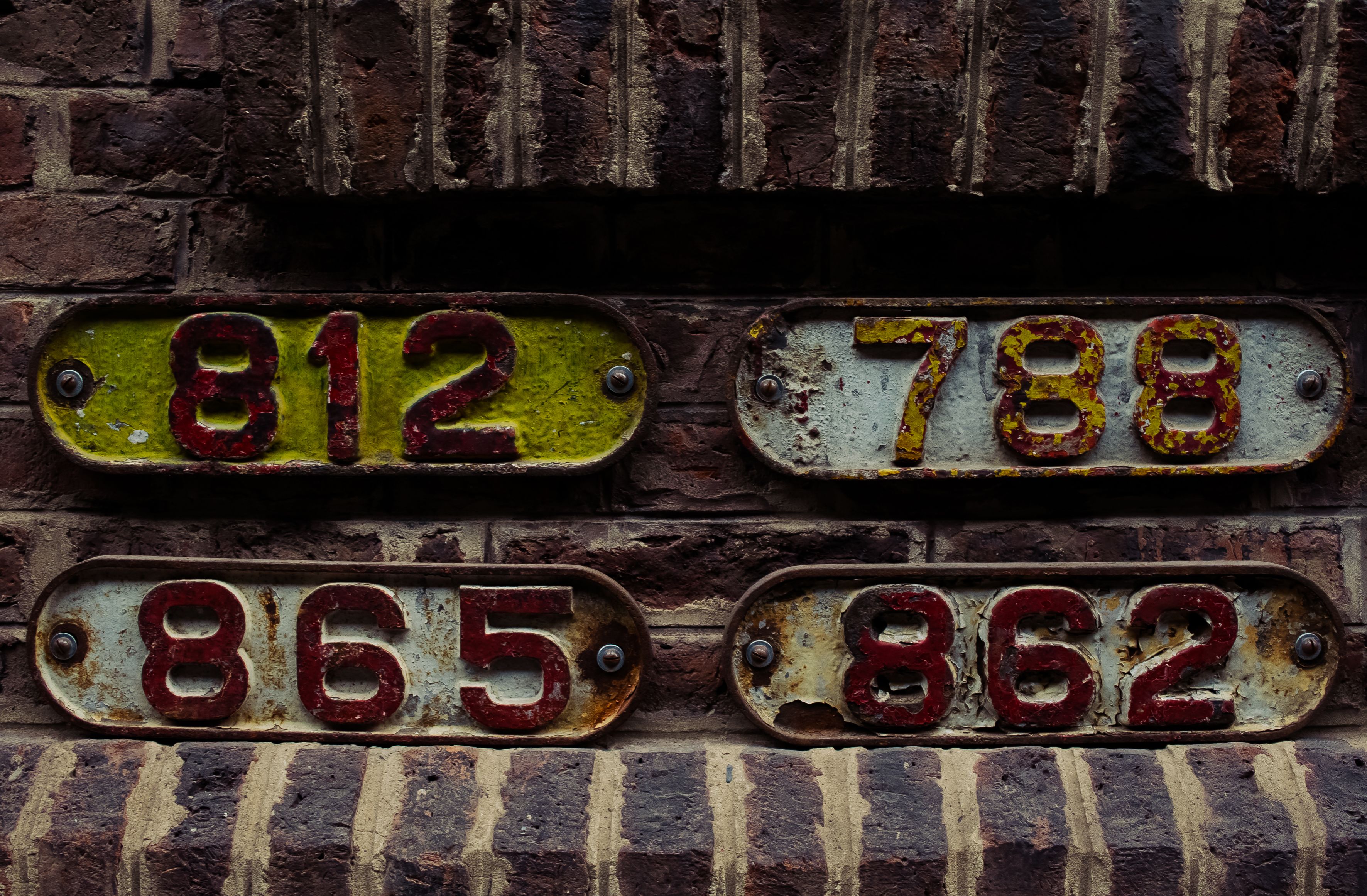 Close-up of vintage, weathered number plates mounted on a textured brick wall.