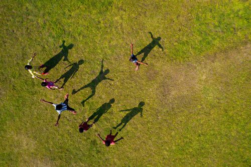 Free A top-down view of children joyfully playing, casting long shadows on a sunlit grass field. Stock Photo