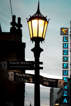Vintage street lamp illuminating direction signs in Buenos Aires at night.