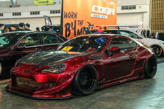 Custom red sports car showcased at indoor auto exhibition featuring striking body kit and modified design.