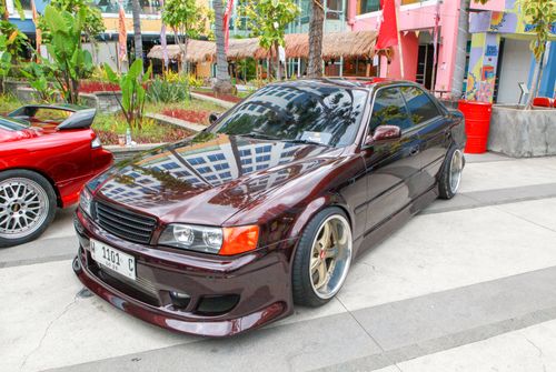 Free A sleek maroon sedan parked on an urban street with tropical plants nearby, showcasing modern car design. Stock Photo
