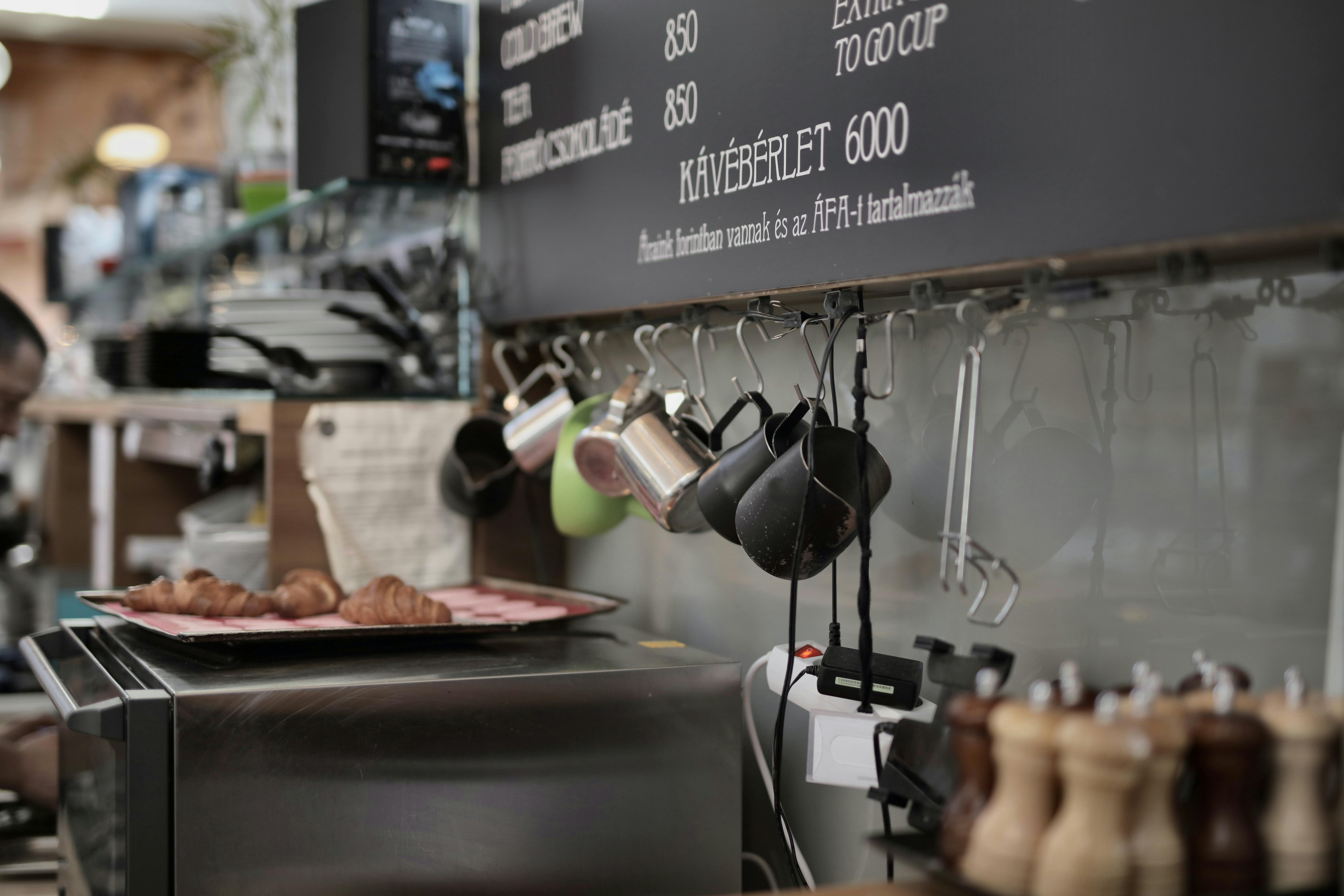 various metal cups hanging on hooks near wall in kitchen of modern cafe