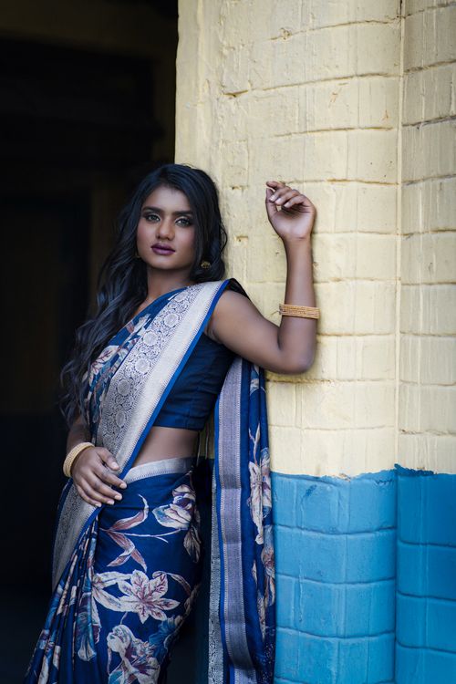 Free Beautiful woman in a blue floral saree posing indoors against a yellow wall, showcasing traditional Indian attire. Stock Photo