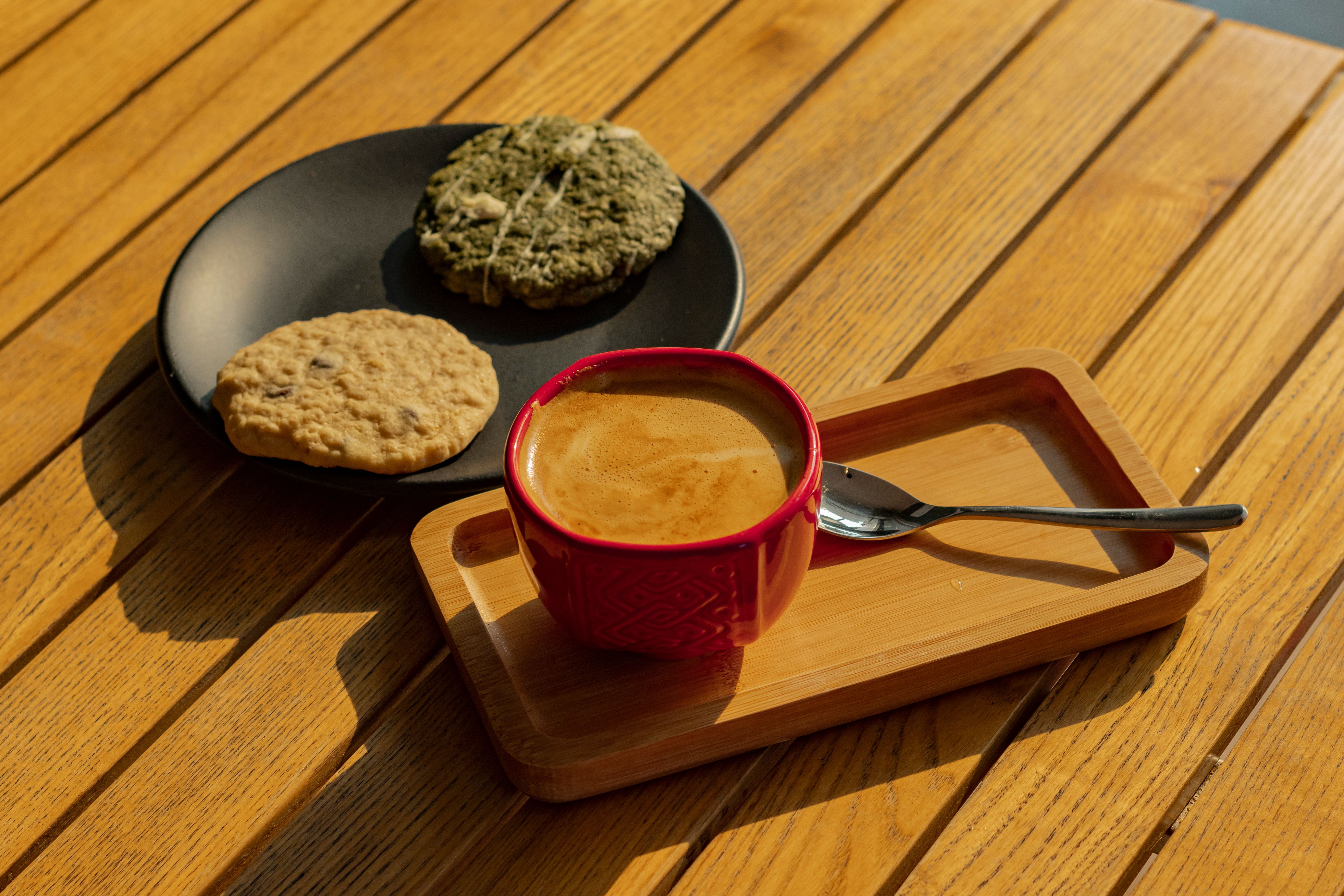 A cup of hot coffee with assorted cookies on a wooden table in warm sunlight.