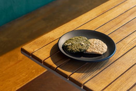 Two cookies on a black plate placed on a sunlit wooden table, creating a cozy cafe ambiance.